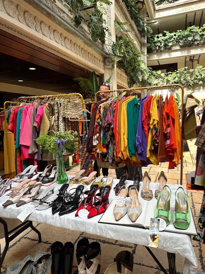 our-mission-01 Vibrant vintage clothing and shoes displayed indoors with lush greenery.