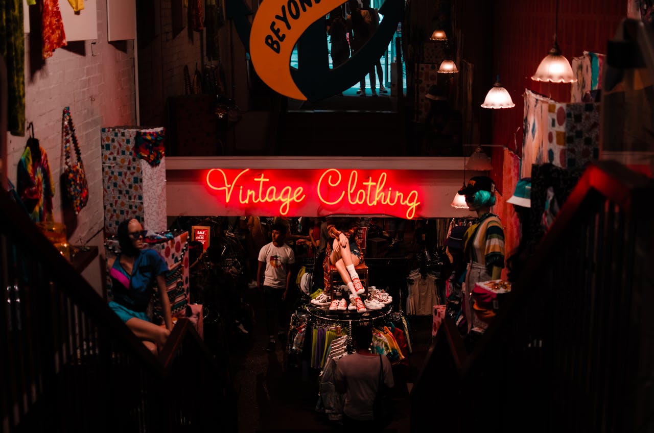 High angle of anonymous person walking down stairs to vintage shop with hangers and mannequins with neon sign